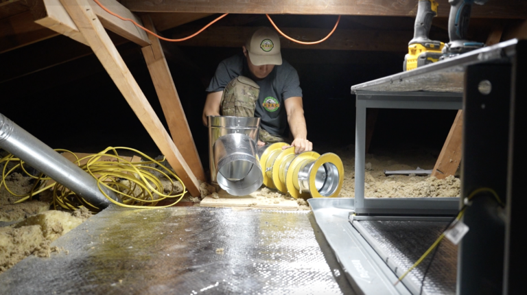 HVAC technician installing flexible ductwork in an attic space during a home ventilation repair.

